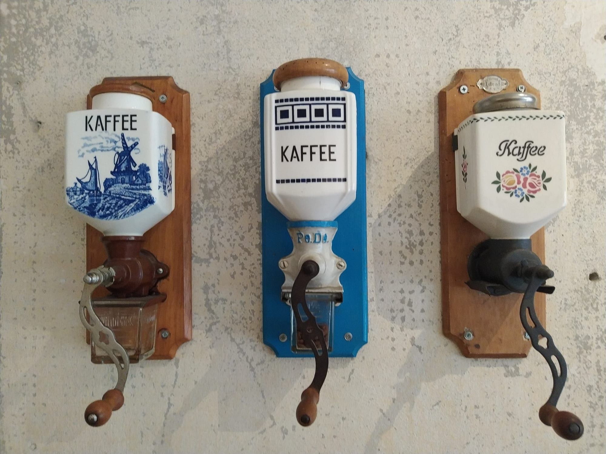 Three vintage wall-mounted hand-crank coffee grinders with ceramic hoppers