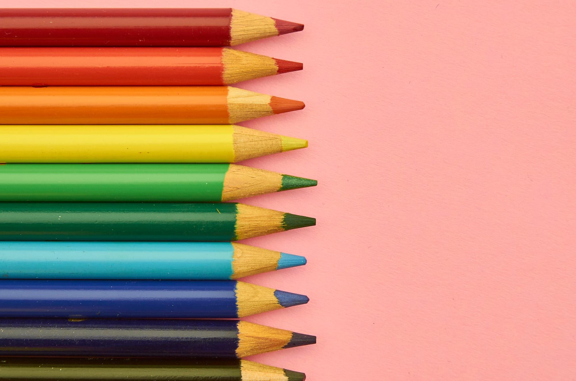 A row of sharpened coloured pencils lined up on a pink background