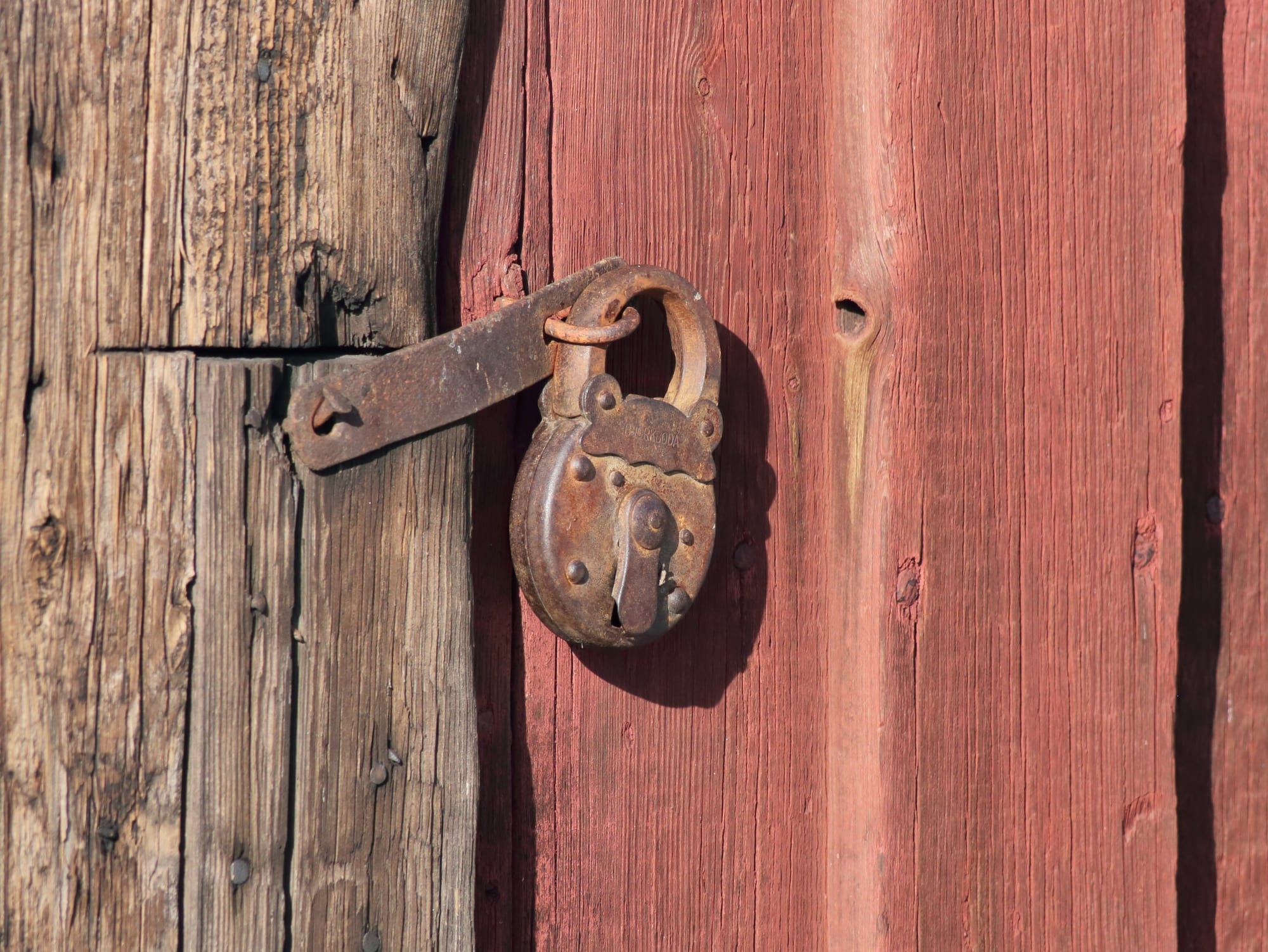 A rusty old padlock hanging on a hasp on a red wooden door