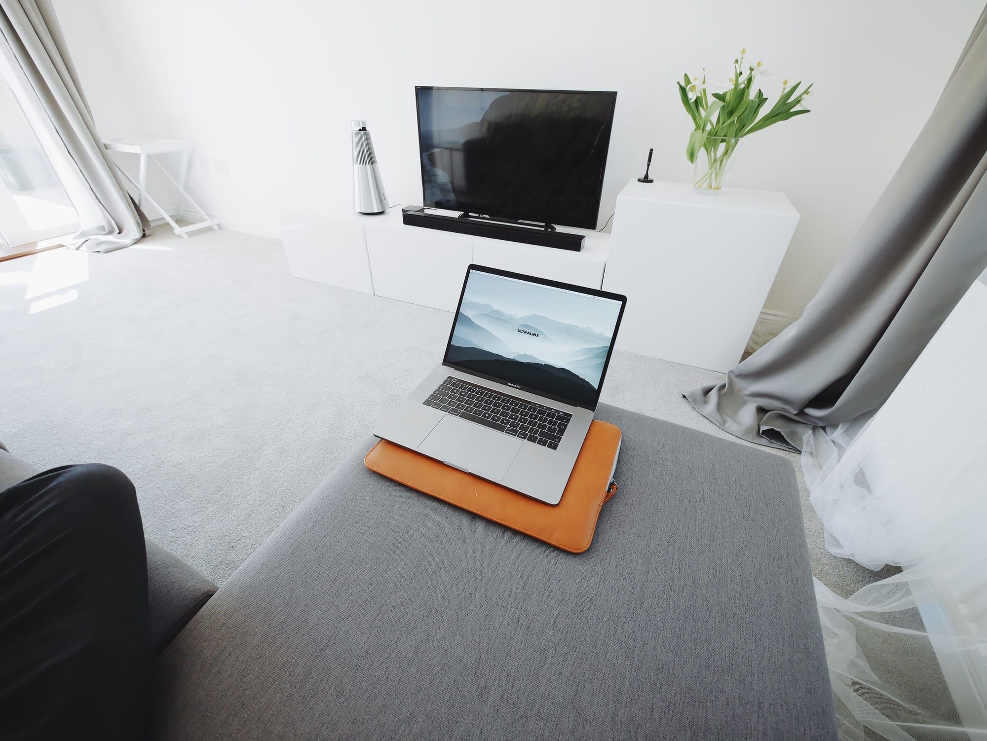 A laptop on a cushion on a sofa in a bright, minimal living room